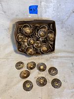 Box containing multiple vintage brass bead caps with textured pattern and central hole, showing aged brass patina.