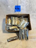 Box with multiple gold-tone Bic lighter covers with embossed skier motif, some wrapped in plastic.