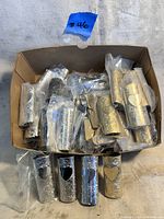 Photo showing multiple vintage metal Bic lighter covers with heart cutouts in a cardboard box, mostly wrapped in plastic.