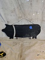 Front view of the full wooden pig shaped rack painted black with white stripe and three hooks.