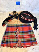 Full view of the tartan kilt with two matching Highland hats on top, showing colors, patterns and ribbons.