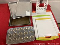 Image showing two small muffin tins, three rectangular baking pans stacked, one bread slicer, and three cutting boards with colored edges.