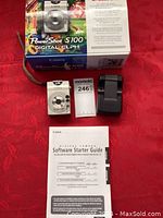 Full lot arranged on red fabric including the camera, box, charger, and manual.