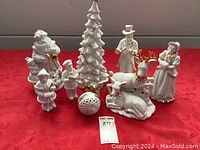 Full view of the ceramic Christmas decorations set on red fabric, showing Santa, carolers, Christmas tree, reindeer, and ornament ball.