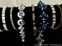 Photo of 6 bracelets on a black velvet display stand showing silver-tone metal and various stones and bead designs
