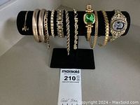 Photo of gold tone costume jewelry bracelets displayed on black jewelry stand showing varied styles including bangles, rhinestone, chain links, and gemstone centerpieces.