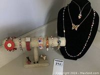 Bracelets displayed on a beige stand with assorted beads and designs; small earrings and ring on stand base; necklaces displayed on black bust form.