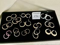 Top view of 12 pairs of pierced hoop earrings on black display board showing different gold tone textures and styles plus pink and silver tone pairs