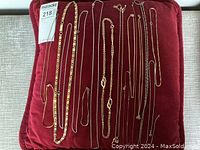 Top view of nine costume jewelry chains on a red cushion showing various gold tone and silver plated finishes and different sizes.