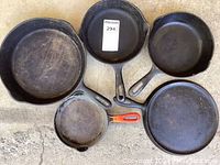 Top view of five cast iron skillets showing worn surfaces and sizes.