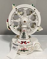 Front view of the white ceramic musical Ferris wheel music box decorated with holiday-themed designs and a central floral motif.