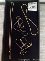 Four gold-tone chains of different thicknesses and styles laid on a black background to highlight the color and clasp types.