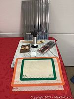Photo showing the marble pastry board, reflective metal stove mat, professional torch, small gold pastry box, pastry tools in packaging, and silicone baking mats on red cloth.