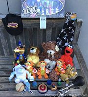 Photo of assorted plush toys including Ty Beanie Babies Tigger, teddy bear, Koala, Garfield, Scooby-Doo holding pizza slice, Elmo, Wizard of Oz PEZ Collector's Series box, hats, baseball, figurines and wooden spin tops on wooden bench