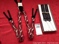 Two sets of Trafalgar formal suspenders laid out on a red patterned fabric surface. One set is deep red with dancers print; the other set is black with white vertical stripes, shown in original box.