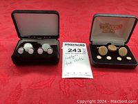 Two sets of tuxedo cufflinks and studs displayed in their individual cases. One set gold tone with yellow enamel, the other silver with mother of pearl.
