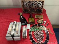 Photo of woven Pottery Barn Havana wine rack, two electric wine openers in boxes, small wine bottle basket, stained glass art pieces, cheeseboard with metal knife, and six glass fish stem decorations on a red tablecloth.