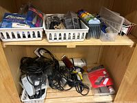 Wide shot of shelving with multiple plastic baskets containing combs, clipper guards, and tools on top shelf; several electric clippers with cords, brushes, and packaged items on bottom shelf.