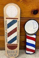 Two barber pole signs side by side against wood background.