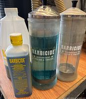 Front view of two Barbicide jars and a bottle of Barbicide disinfectant solution on a wooden surface.