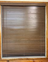 Front view of brown wooden horizontal blinds installed inside wooden window frame.
