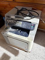 Front view of the Brother color laser printer showing the control panel, output tray, power cord and dirt on top surface.