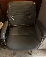 Front view of vintage wash station chair showing padded vinyl seat and backrest with plastic cover, metal frame with rust on legs, and padded armrests.