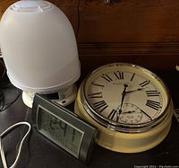 Clocks shown together on flat surface; large analog wall clock with beige frame and Roman numerals, digital clock displaying 12:41, and white dome covering smaller clock.