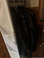 Clothes rack with several dark jackets and shirts hanging on hangers behind a white fabric organizer