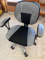 Front and side view showing the fabric upholstery on seat and backrest with armrests and caster wheels on metal base.