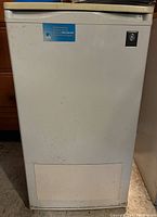 Closed view of small white GE refrigerator showing front door with GE logo and a sticker.