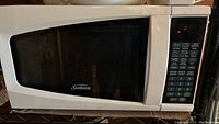 Front view of the white Sunbeam microwave showing door, control panel with numerous buttons, and brand logo.