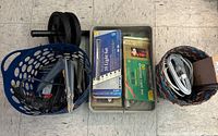 Photo showing three baskets containing items: blue ab roller, black electric drill, boxed 35-light professional series light set, box of zip ties, extension cords, and miscellaneous items.