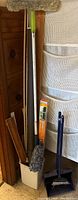 Photo showing mop, gray sponge mop, wooden trim pieces, and cleaning items leaning against door frame.