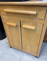 Front view of the wood cabinet showing one drawer and two doors with wooden handles, and visible white marks or scratches under the drawer.