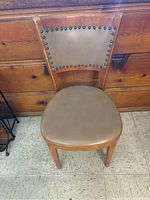 Front view of wooden chair showing padded beige upholstered seat and backrest with metal stud detailing.