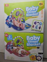 Box showing two different colored baby fitness blankets with multi-function play mats and sensory toys