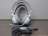 White Fantech HG11 gaming headphones standing upright showcasing cushioned ear cups, headband, attached microphone, and USB braided cable with in-line volume control on neutral background.
