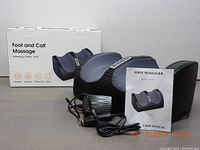 Foot and calf massager device with user manual, power adapter and car adapter, in front of product box showing features and image of device.