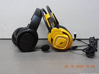 Two wired gaming headsets placed side by side on a table; one black and one yellow with black accents, showing ear pads and microphones.