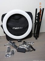 Full kit overview showing LED ring light, tripod stand folded, power adapter, mounts, and carrying bag.