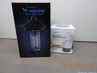 Photo showing the boxed items: Palone Electric Bug Zapper and Aparotoo Light Column Mosquito Killing Lamp on a flat surface.