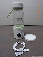 Portable bottle warmer and glass baby bottle with white lid placed on warming base along with USB charging cable.