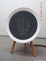 Front view showing white circular heater with black mesh grille and wooden tripod legs.