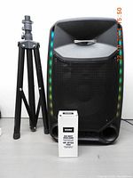 Front view of ION Total PA Ultimate portable speaker with colorful LED edge-glow lights next to folded tripod stand and boxed microphone.