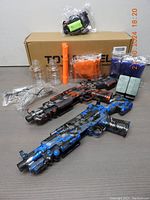 Full set layout showing both gel ball blasters, goggles, charger, magazines, bottles, and accessories in front of cardboard box