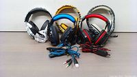 Photo showing all 5 gaming headsets arranged side by side, including white/black, blue, yellow striped, red/black, and gray camouflage designs with their cables coiled in front.
