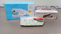 Photo of three handheld electric sewing machines, showing different models and packaging.