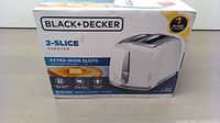 Front box view showing Black & Decker branding, '2-Slice Toaster' label, extra-wide slots feature, seven heavt toast settings, cancel button, and high-lift lever.