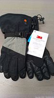 Front view of gloves showing black and gray exterior, adjustable wrist strap, and 3M Thinsulate tag attached